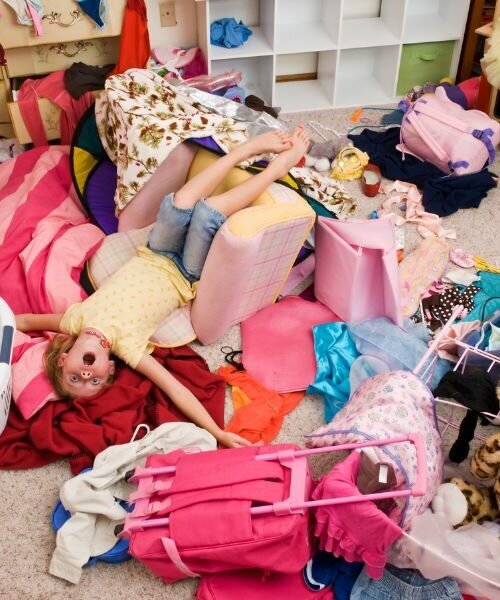 this is a photo of a very cluttered kid's room with a child laying in the middle of it