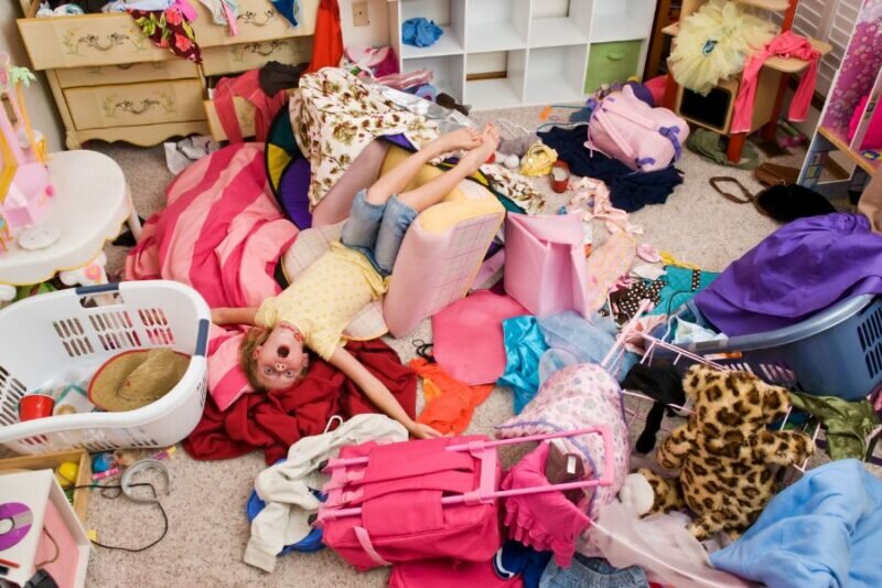 this is a photo of a very cluttered kid's room with a child laying in the middle of it